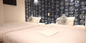 A hotel room with two beds, each with a white bedspread and matching pillows. The wall behind the beds features a blue and black floral wallpaper pattern. - Hotel Art Inn Namba (Osaka)