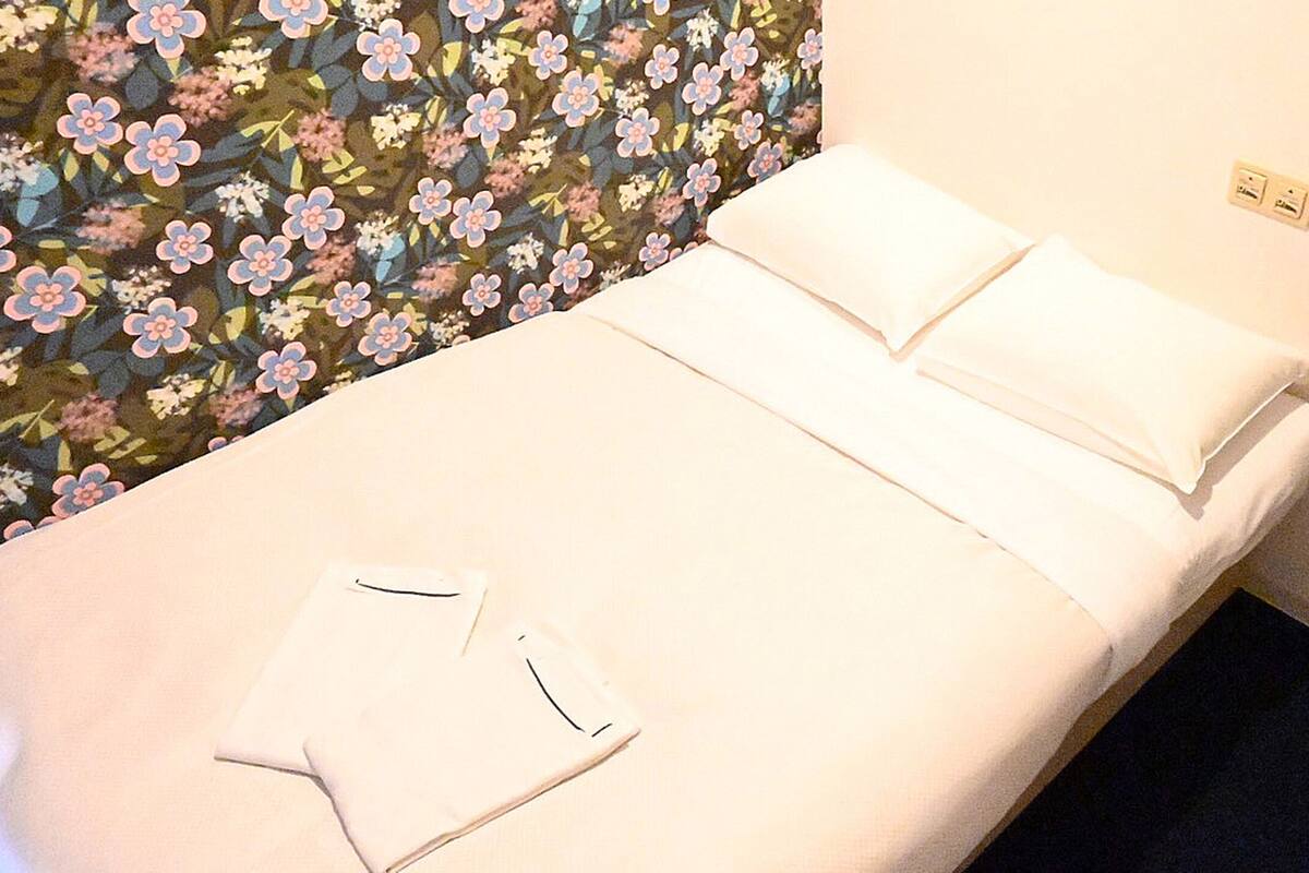 Un letto singolo con lenzuola bianche in una stanza con carta da parati a motivi floreali.