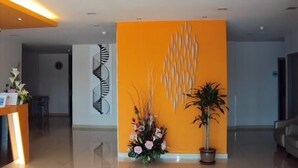 A modern reception area with a bright orange accent wall, a decorative wall piece, and a floral arrangement. - GM City Hotel (Klang)