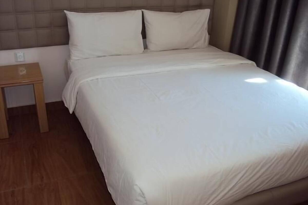 A neatly made bed with white linens, a wooden nightstand, and a headboard with a padded design.