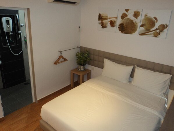 A hotel room with a bed, a small table with a plant, a towel rack, and a wall-mounted air conditioning unit. - GM City Hotel (Klang)