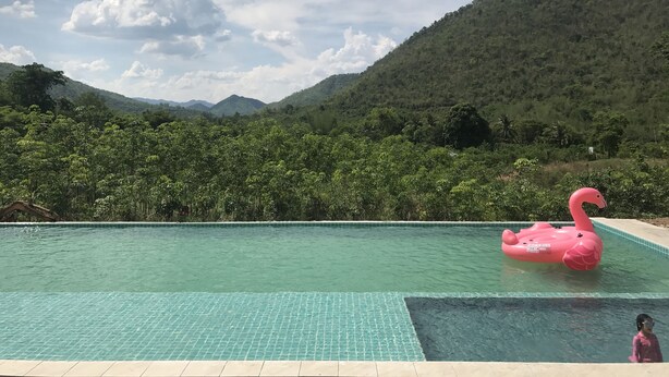 A swimming pool with a pink flamingo float, surrounded by lush greenery and hills. - Hi - Scene Resort (Suan Phueng)