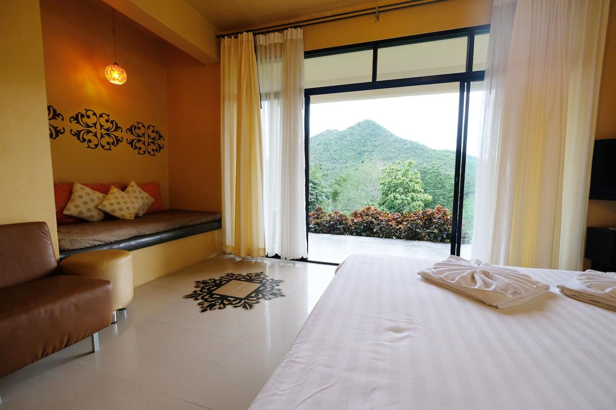 A hotel room with a bed, a sofa, a window with a mountain view, and a decorative wall piece.