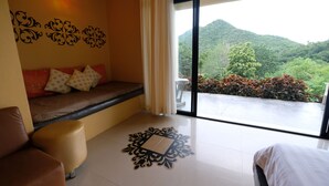 A room with a large window, a sofa with cushions, a small table, and a decorative wall piece. - Hi - Scene Resort (Suan Phueng)