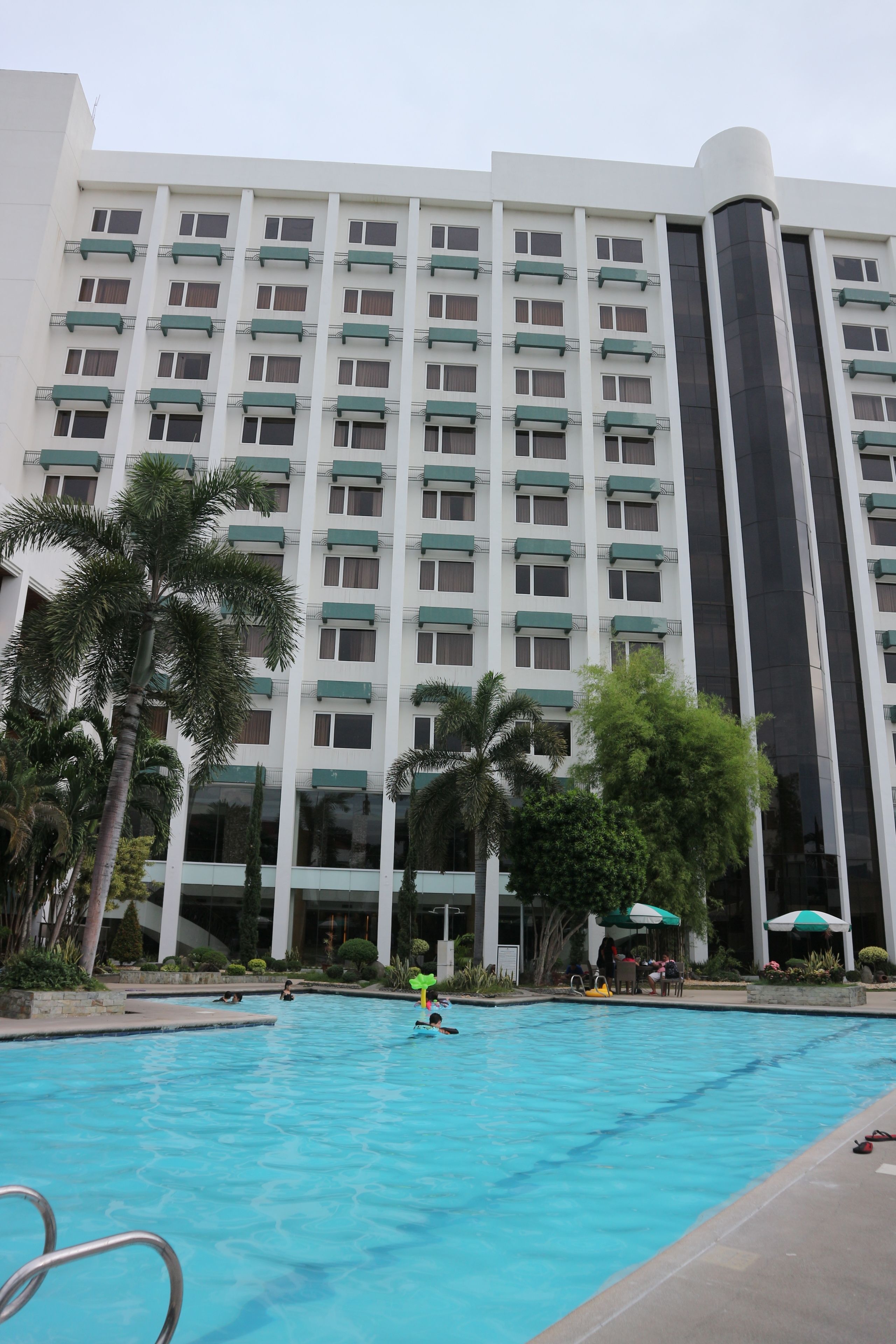 Un hotel con piscina, palmeras y un edificio alto con muchas ventanas.