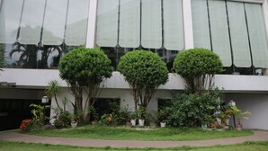 Un bâtiment doté de grandes fenêtres et d’un jardin bien entretenu, où l’on trouve diverses plantes et arbres.