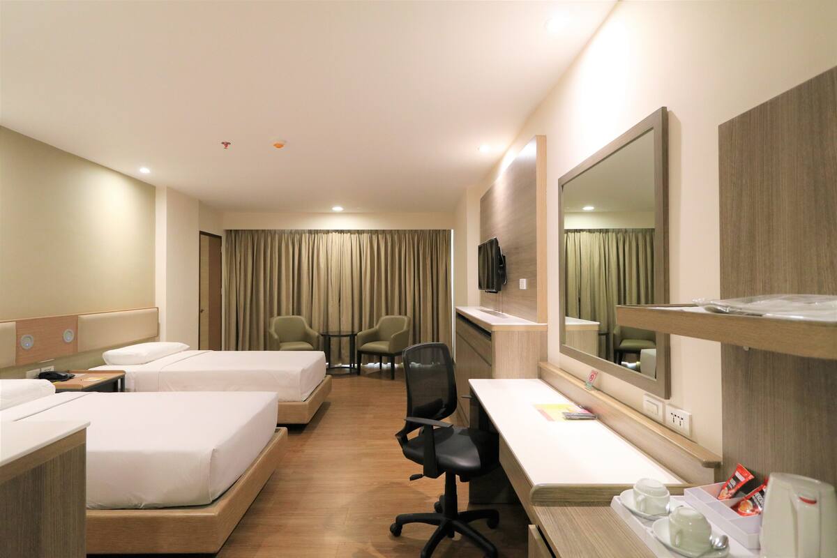Een hotelkamer met twee bedden, een bureau, een stoel, een televisie en een grote spiegel.