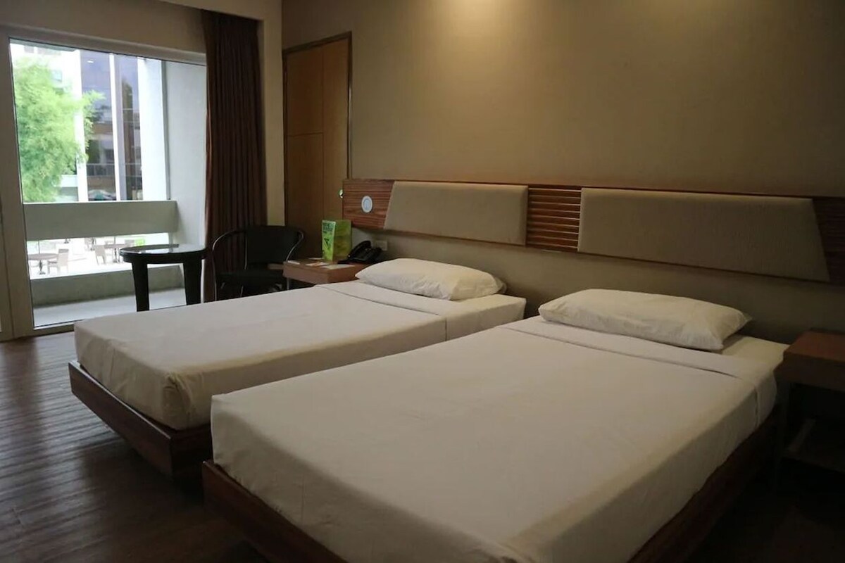 Une chambre d’hôtel avec deux lits simples, un bureau, une chaise et une grande fenêtre.