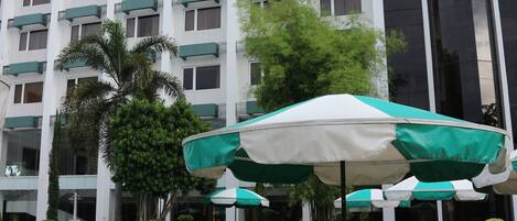 A hotel pool area with outdoor seating and a large building in the background.