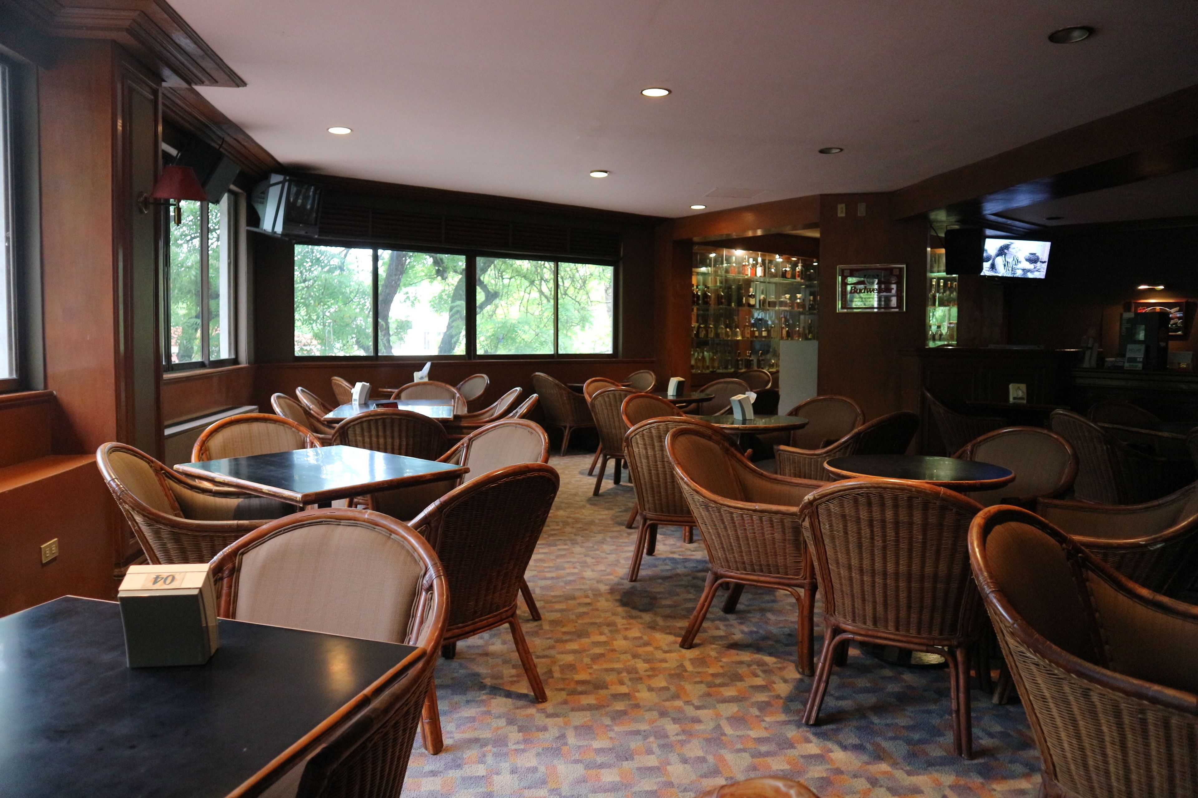 A restaurant with wicker furniture, a patterned carpet, and a bar area with a television.
