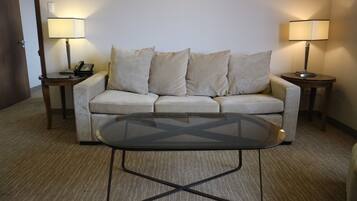A hotel room with a beige sofa, two bedside tables with lamps, and a glass coffee table.