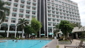 Un hôtel doté d’une grande piscine, d’un espace extérieur aménagé et de palmiers.