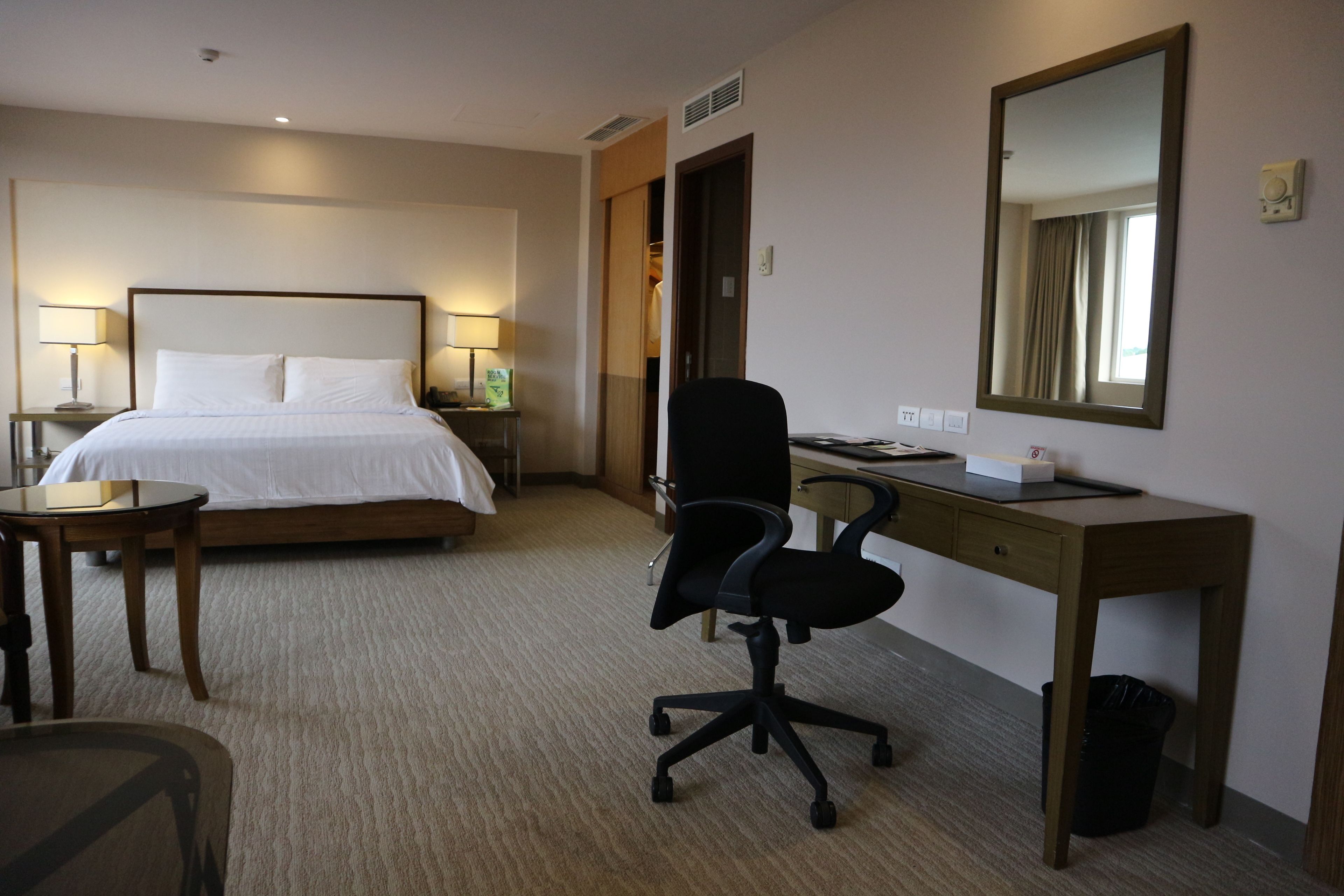 A hotel room with a bed, desk, chair, and a mirror.
