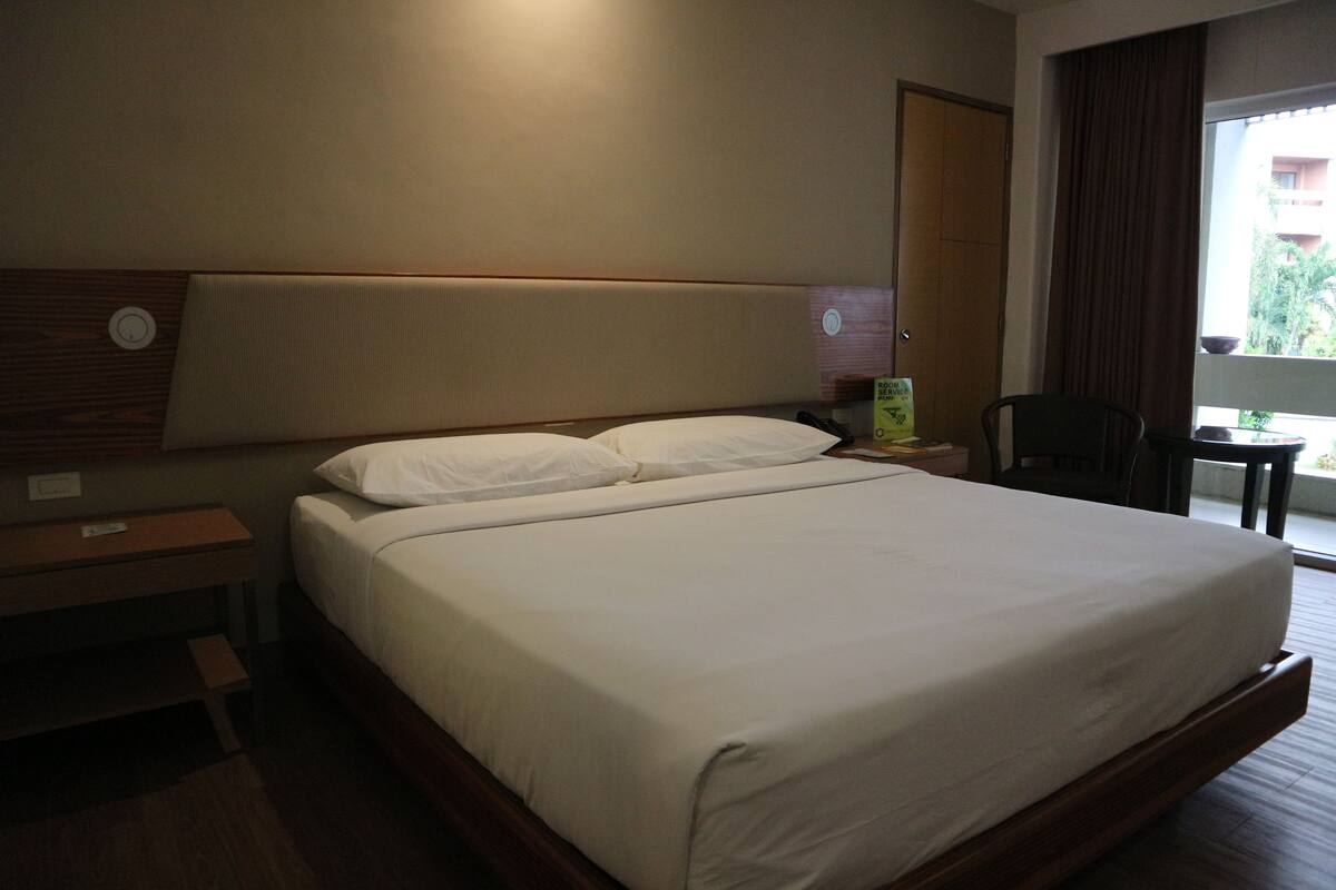 Een hotelkamer met een groot bed, een nachtkastje, een stoel en een raam met gordijnen.