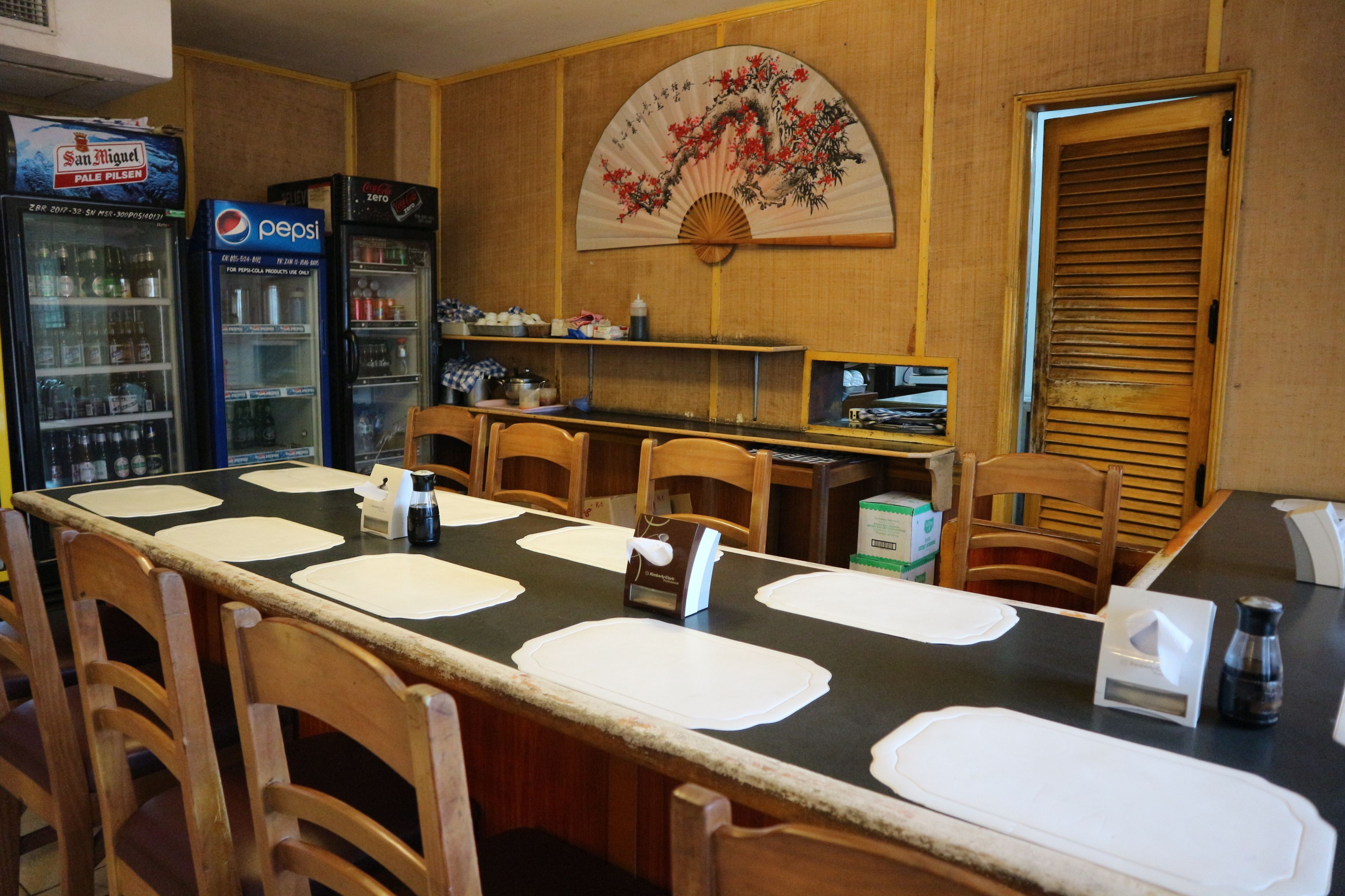 A dining area with a long table, chairs, a fan, and vending machines.