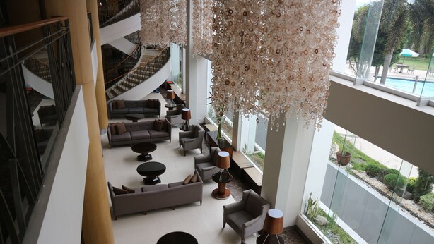 Un hall d’entrée spacieux au design moderne, comprenant un espace de détente central avec des canapés et des fauteuils, un escalier et une vue sur l’espace extérieur abritant la piscine.
