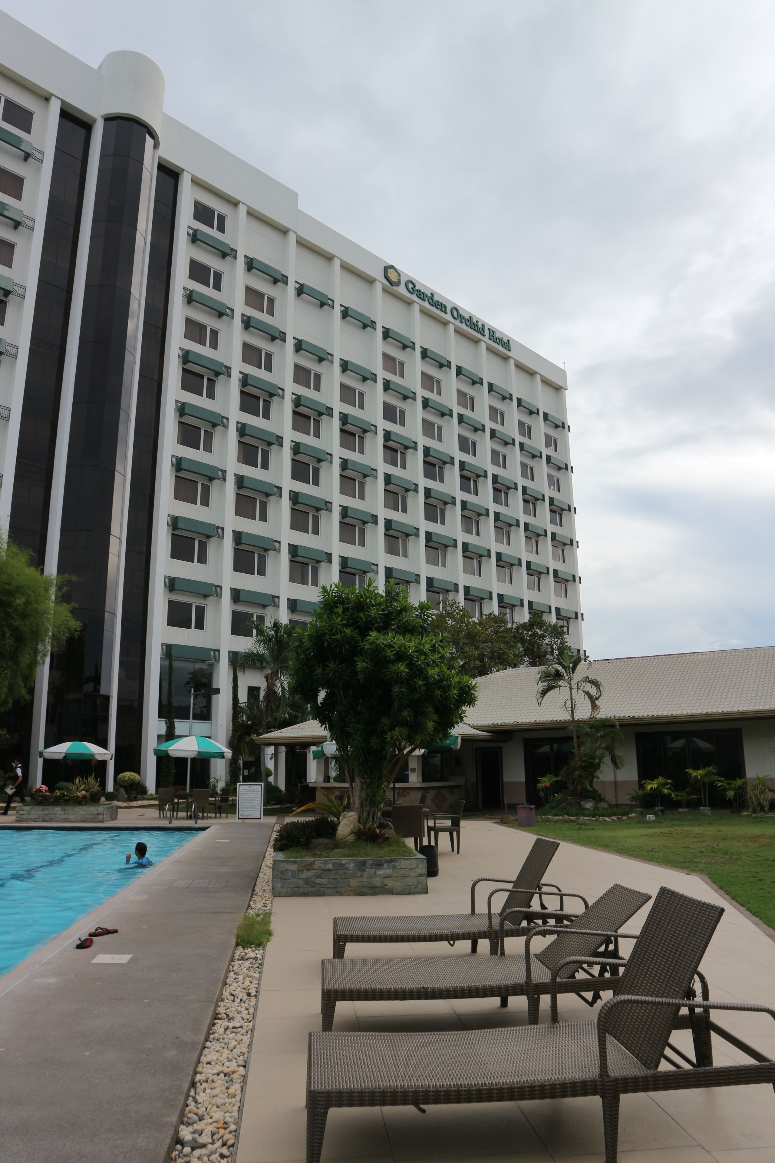 A hotel with a swimming pool, lounge chairs, and a garden area.