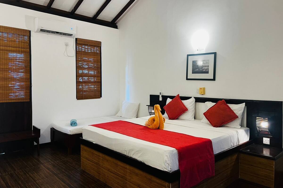 Una habitación de hotel con una cama, una mesita de noche, una lámpara, un aire acondicionado instalado en la pared y un cuadro enmarcado.
