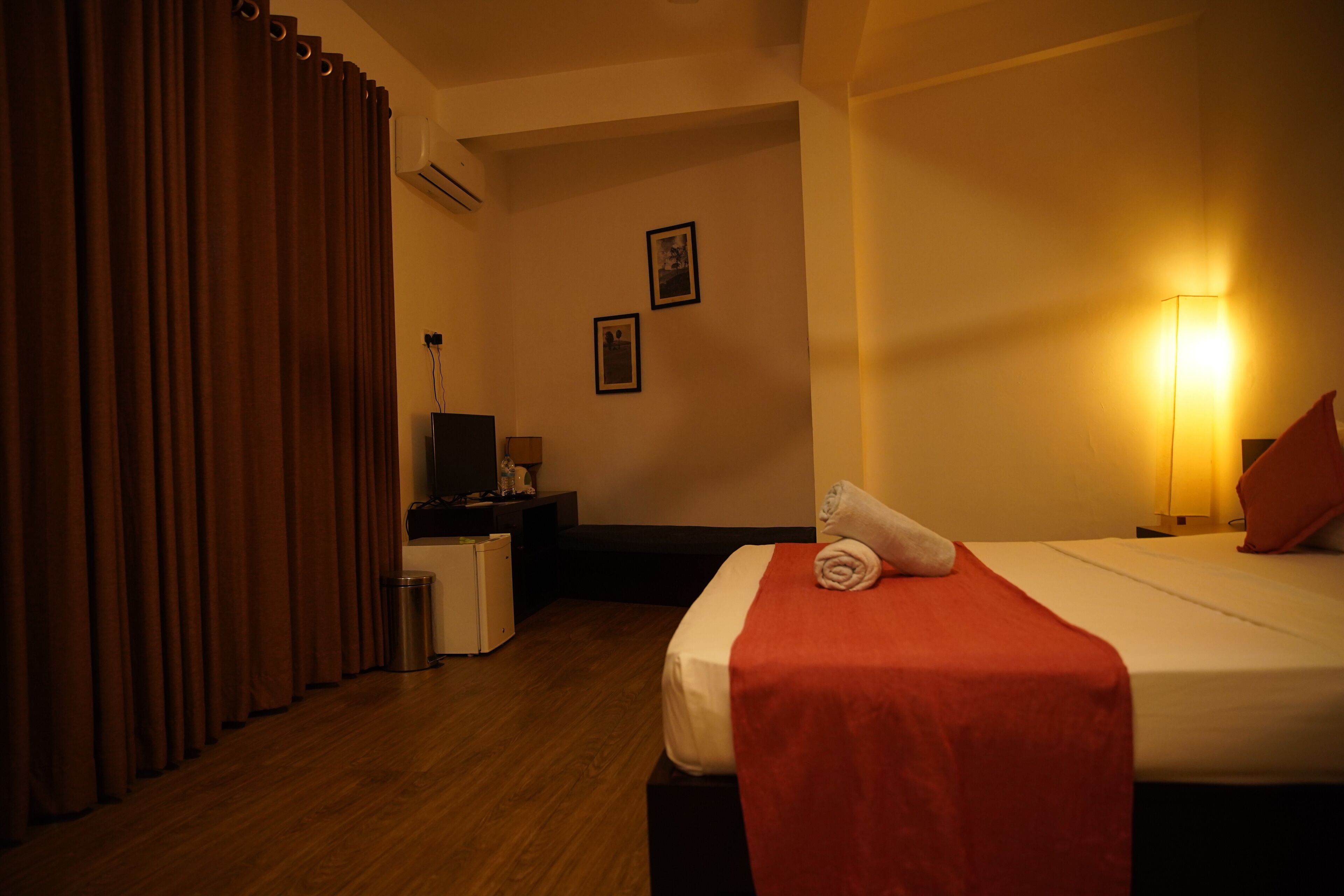 A hotel room with a bed, a desk, a chair, a trash bin, and a wall-mounted air conditioner.