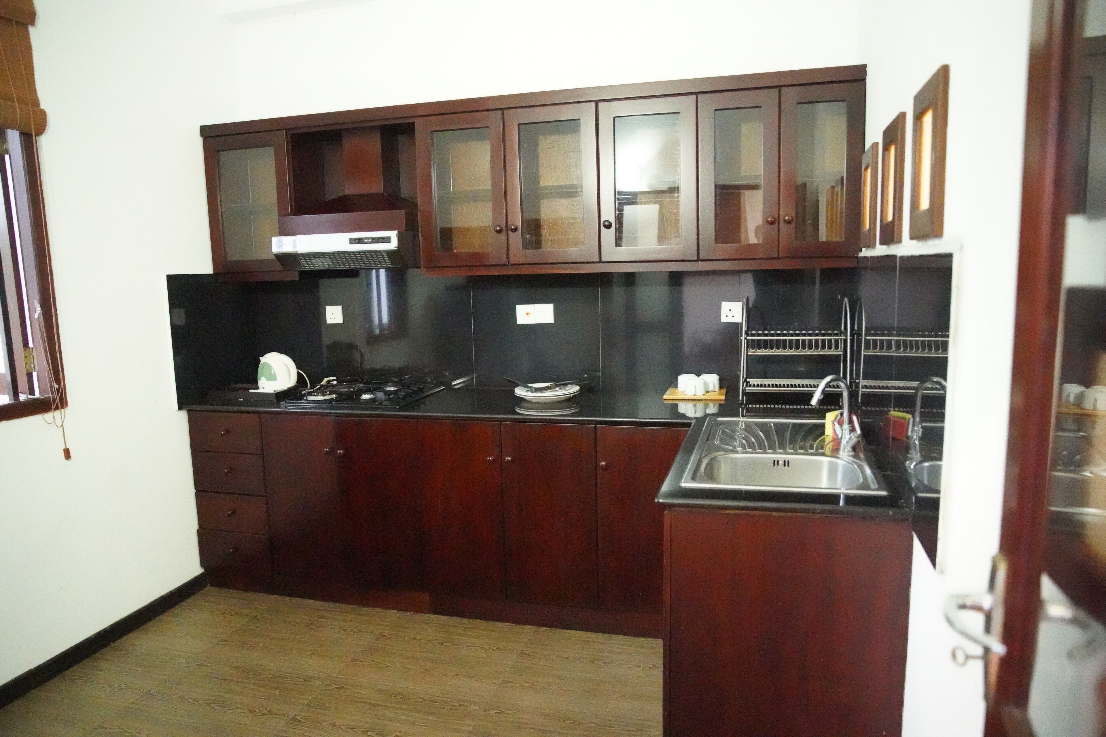 Cocina compacta con armarios de madera oscura, un lavamanos de acero inoxidable y una encimera negra.