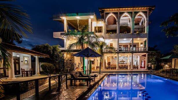 A multi-story hotel with a swimming pool, outdoor seating, and a well-lit patio area. - Fort Edge Retreat (Unawatuna)