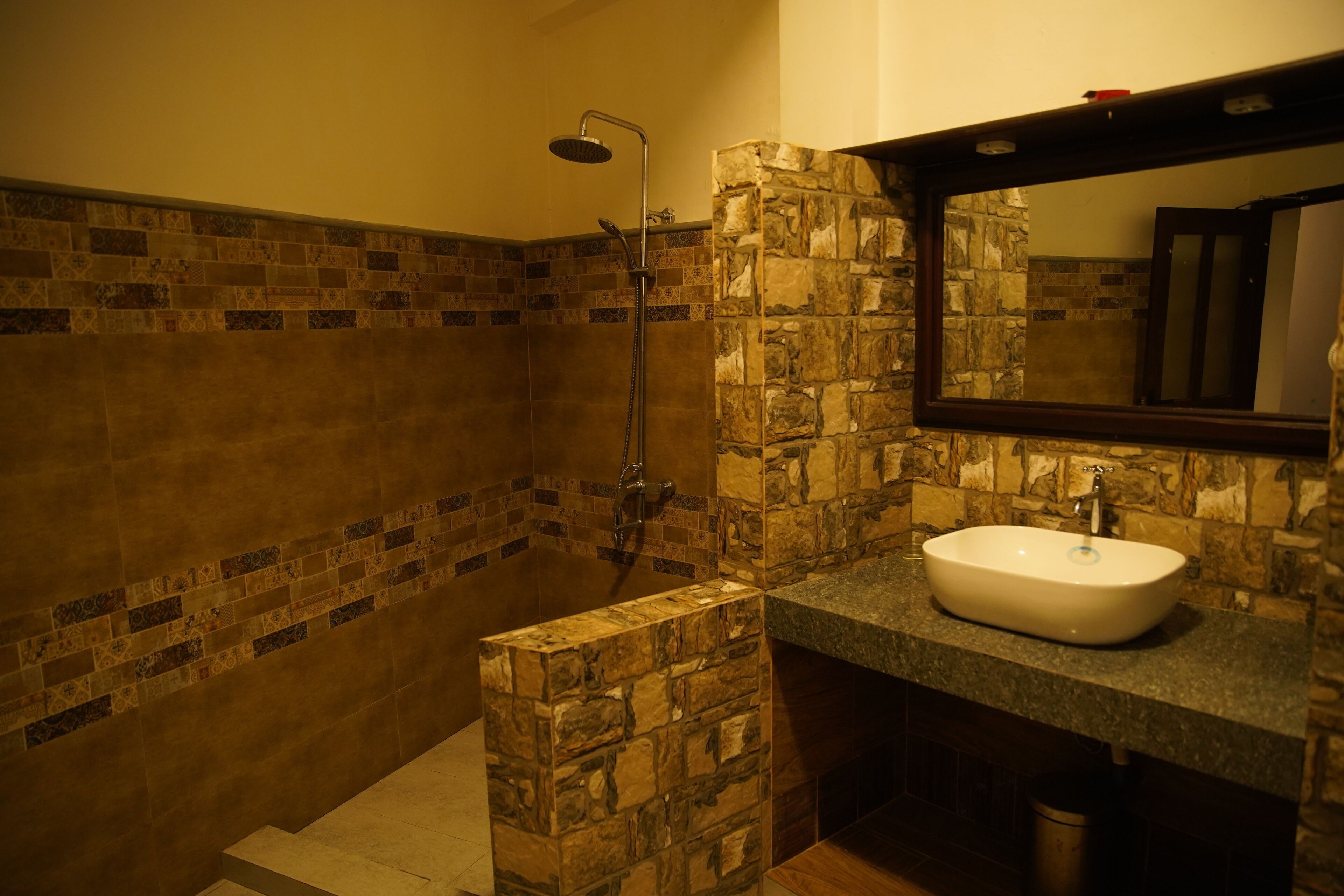 A bathroom with a stone wall, a shower, and a sink with a mirror above it.