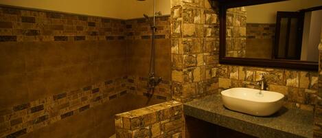 A bathroom with a stone wall, a shower, and a sink with a mirror above it.