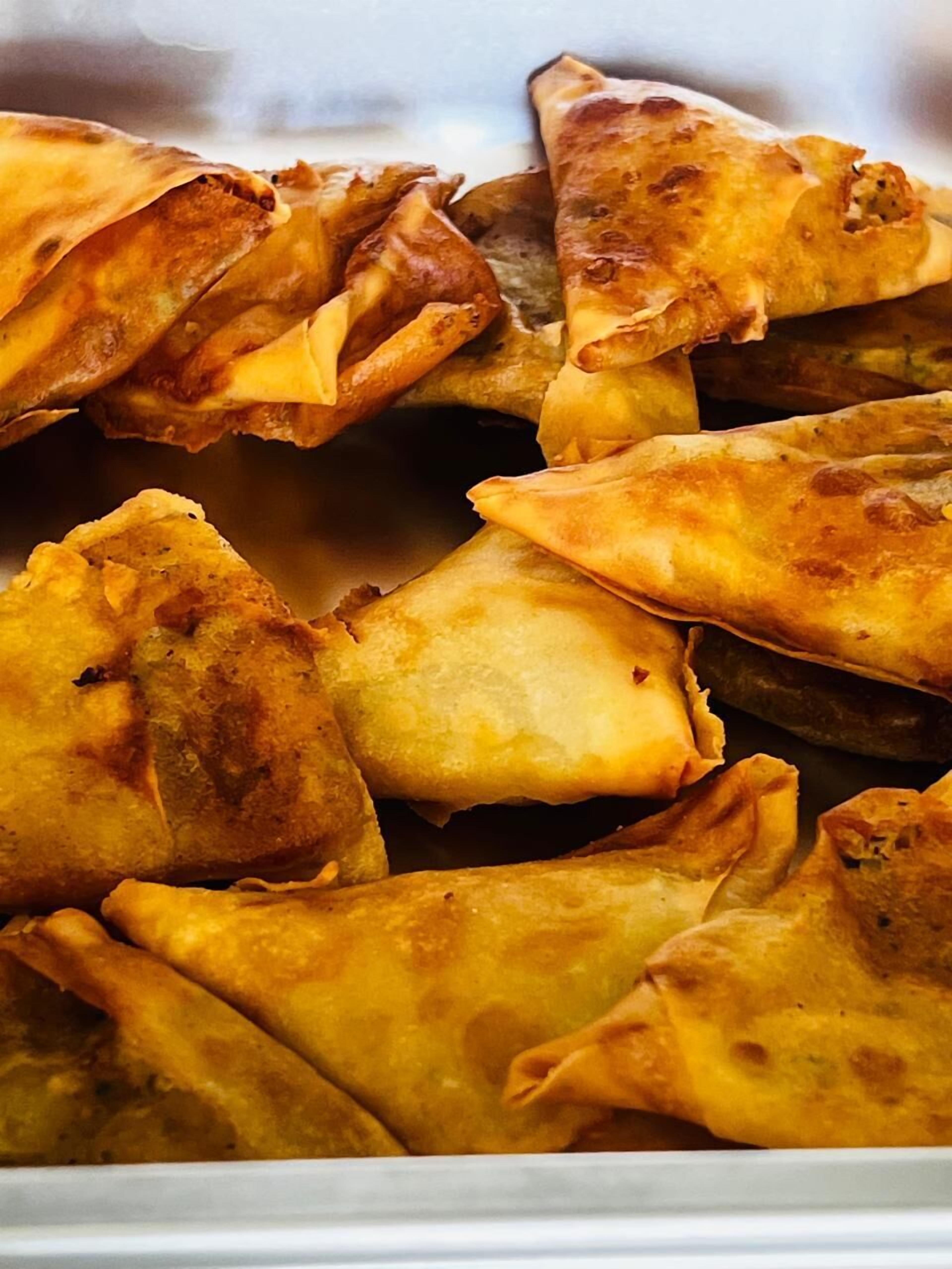 Um close-up de um prato com pastéis dourados e estaladiços, provavelmente samosas, dispostos sobre um prato branco.
