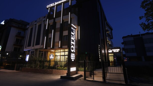 Un hotel moderno con un cartel llamativo que dice "OTEL BUSINESS PALAS" y una entrada bien iluminada.