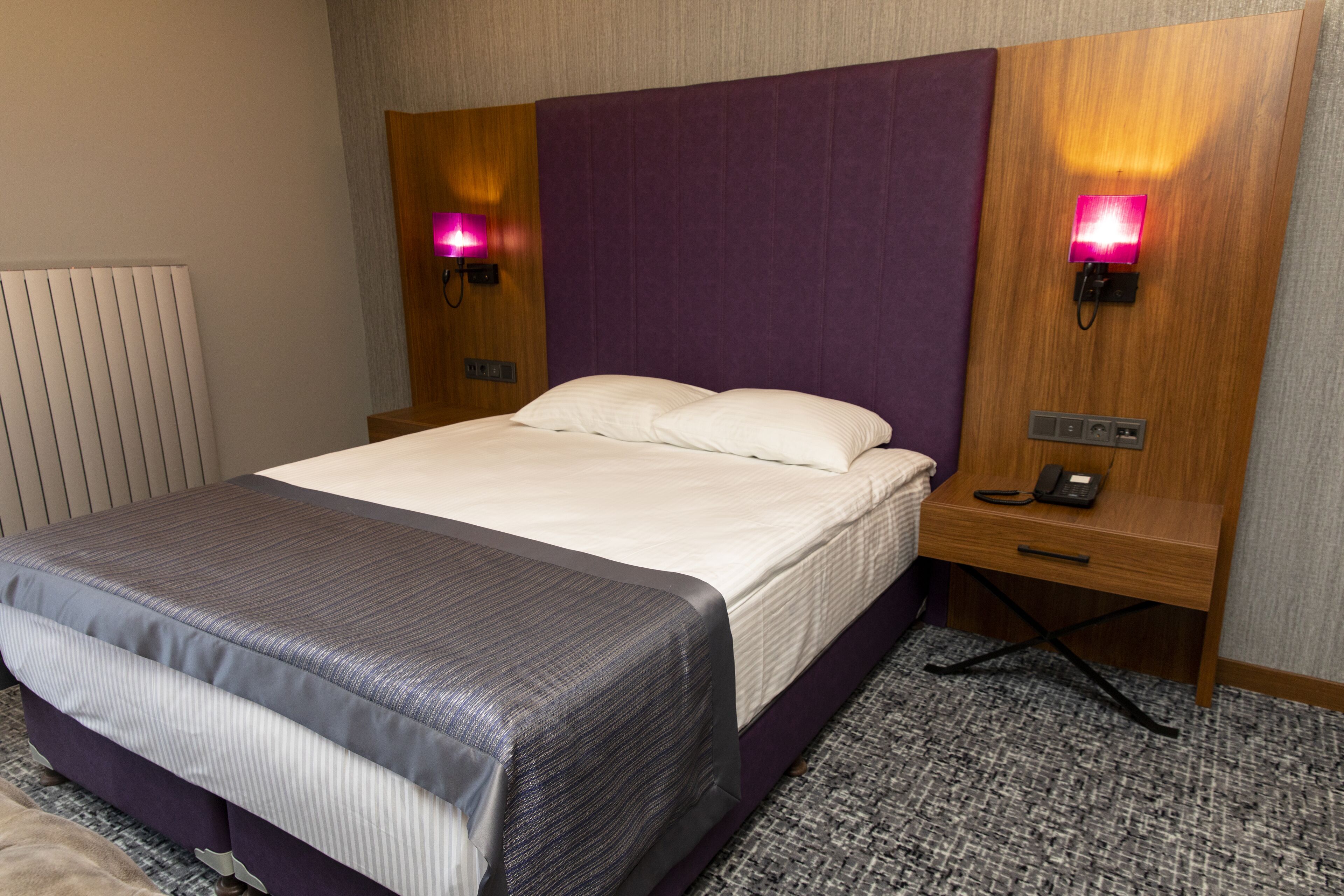Una habitación de hotel con una cama, una mesita de noche, una lámpara y un termostato.