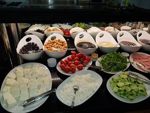 Un bufé con diversos alimentos, incluyendo queso, tomates, pepinos y otras verduras.