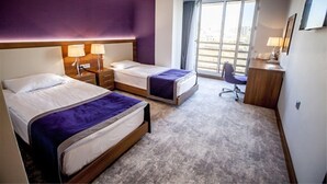 Habitación de hotel con dos camas, un escritorio y una silla. Se ve una ventana con vistas al exterior.