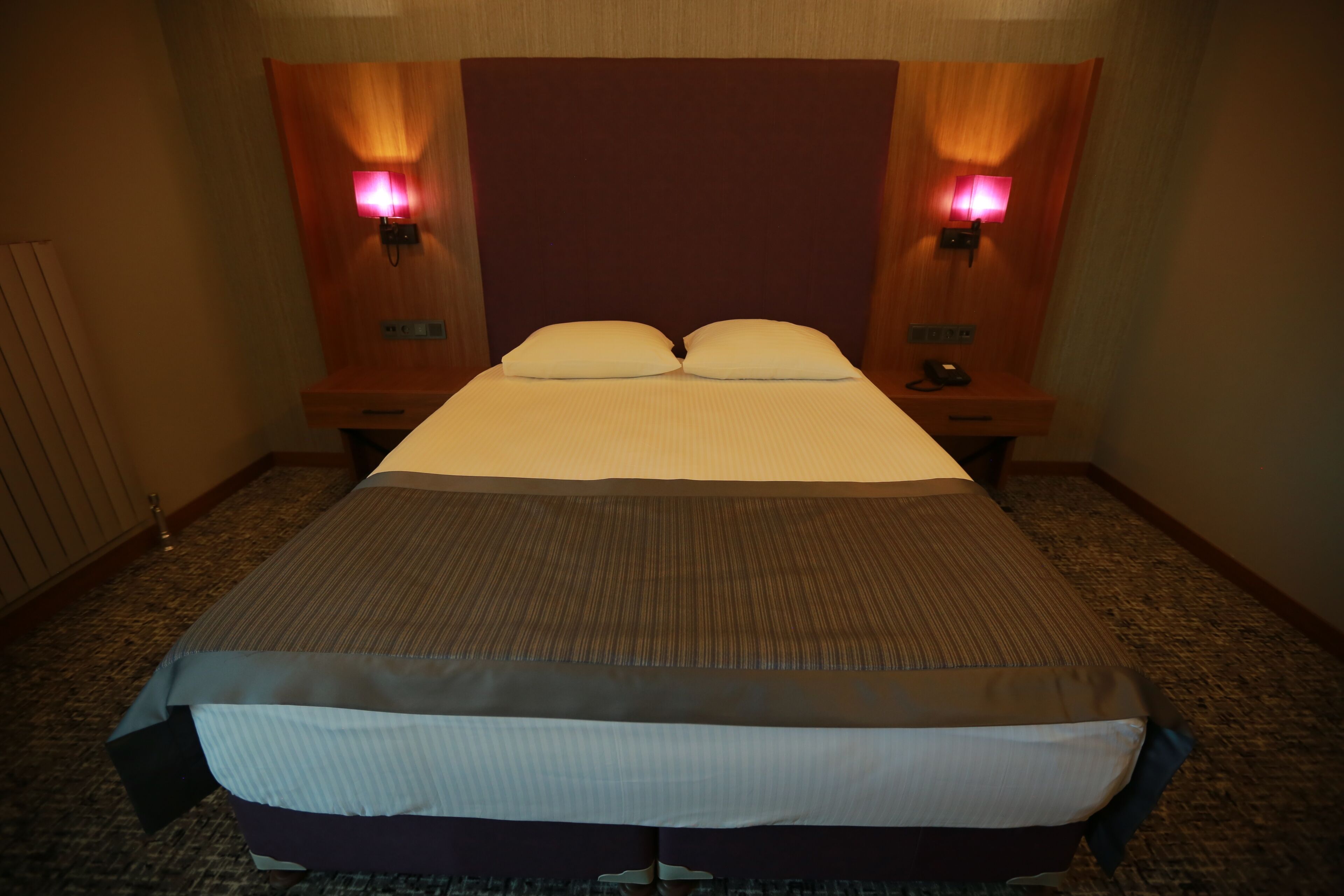 A hotel room with a large bed, two bedside lamps, and a headboard.