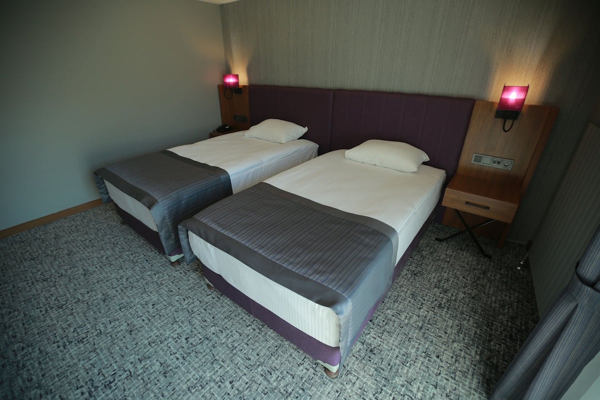 A hotel room with two single beds, a carpeted floor, and bedside lamps.