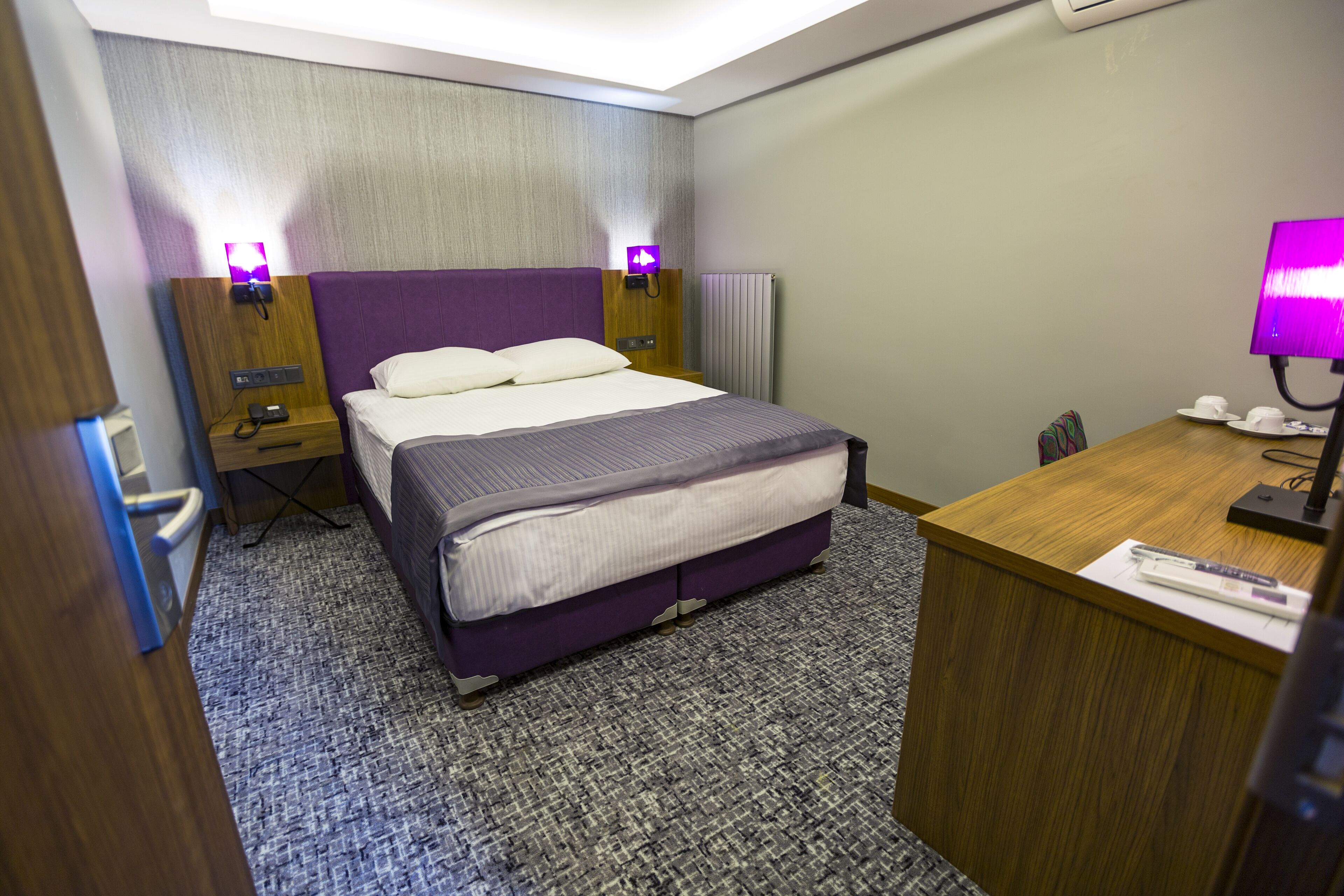 A hotel room with a bed, nightstands, a desk, and a lamp.