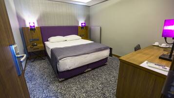 Habitación de hotel con cama, mesitas de noche, un escritorio y una lámpara.