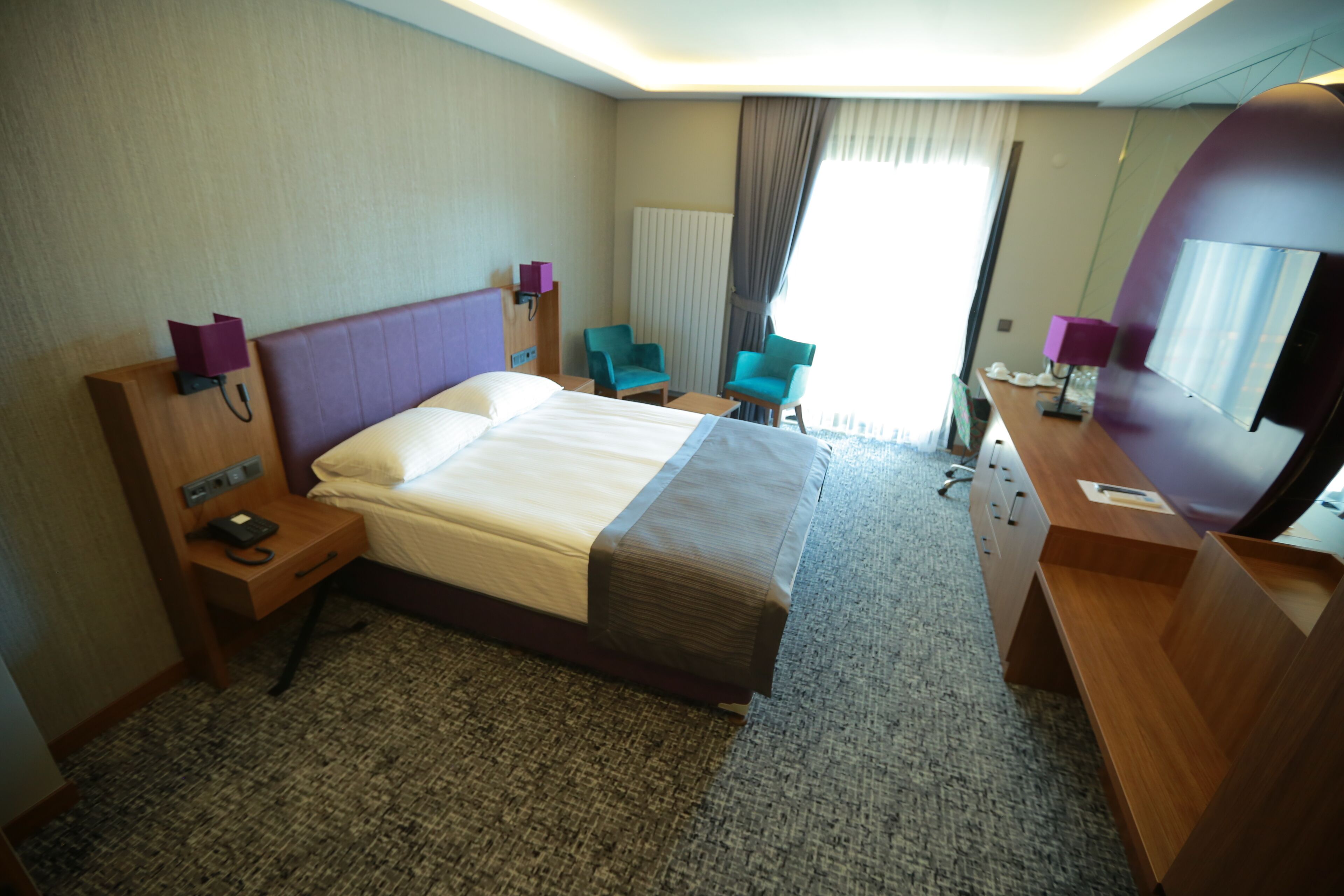 A hotel room with a large bed, two chairs, a desk, a telephone, and a mirror.