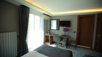 Quarto de hotel com cama, escrivaninha, cadeira, televisão e porta.