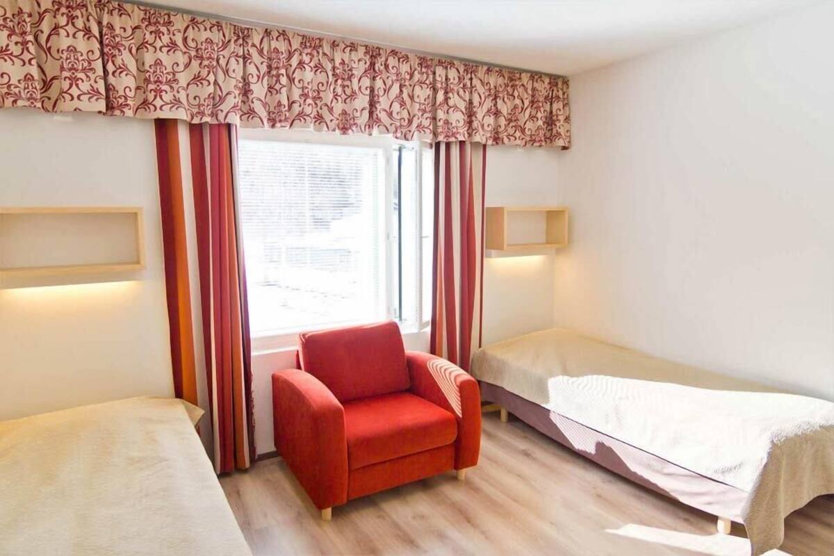 A room with two beds, a red armchair, and a window with curtains.