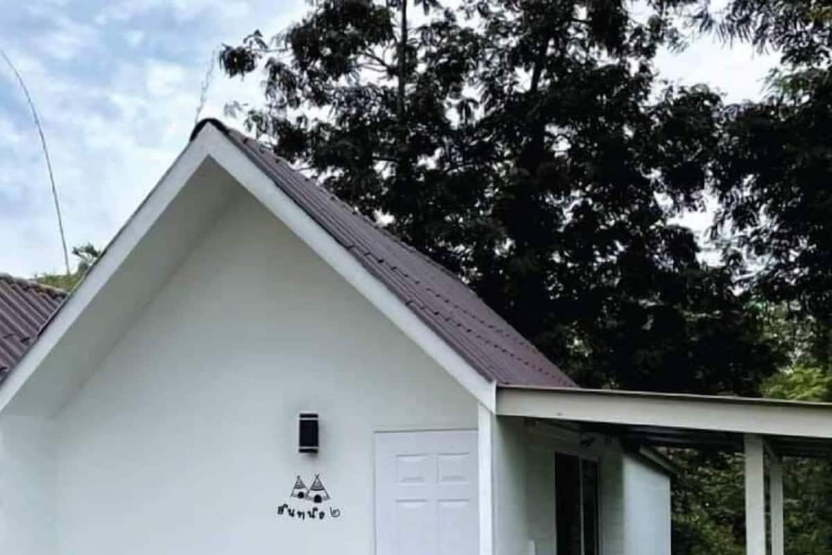 A white building with a sloped roof, a door, and a small porch with potted plants.