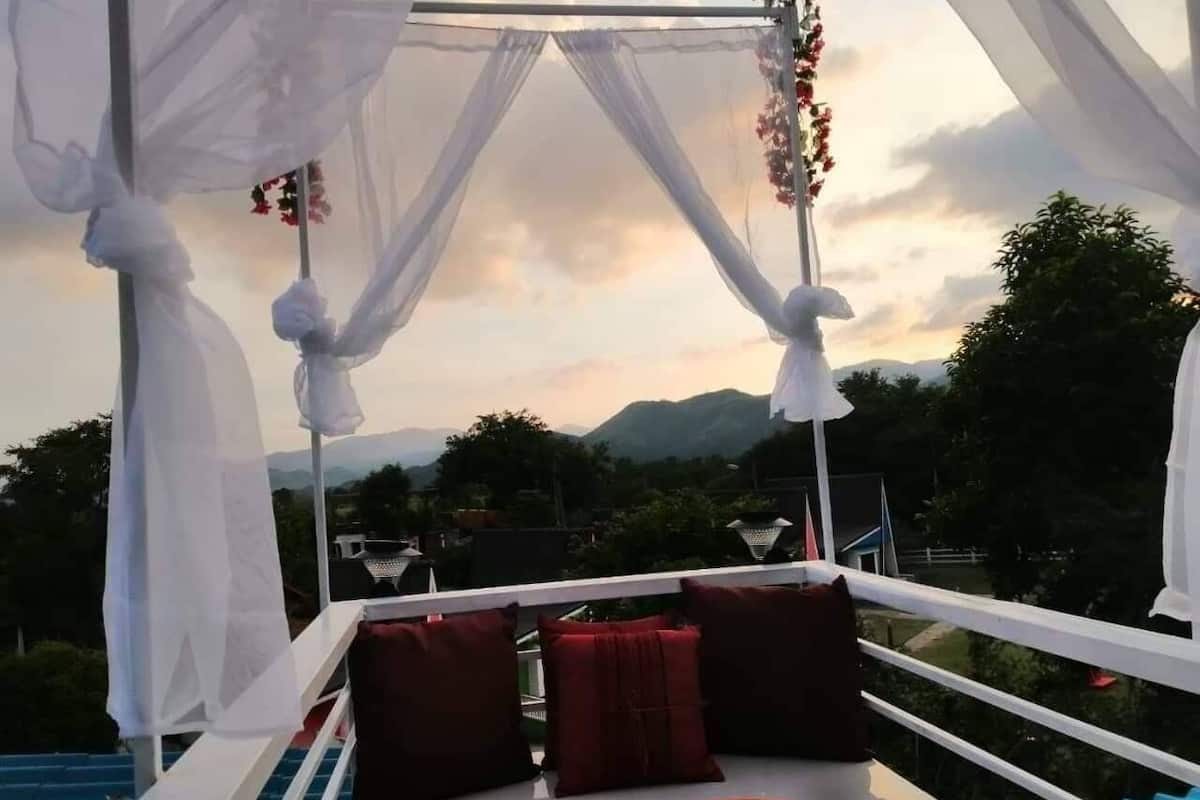 A balcony with a white canopy, red cushions, and a view of mountains.