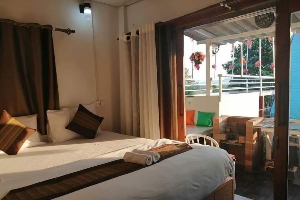 A hotel room with a bed, a small table, and a view of the outdoors.