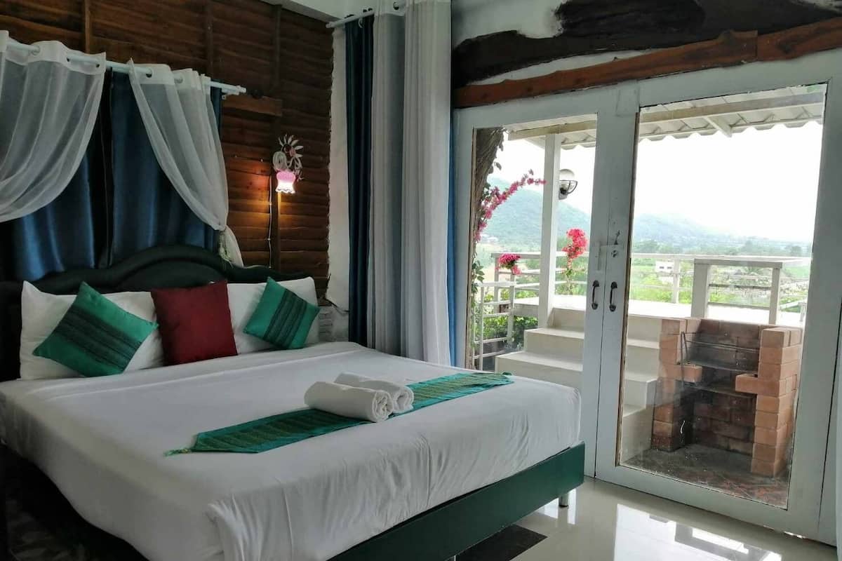 A hotel room with a large bed, a balcony with a view, and a wooden ceiling.