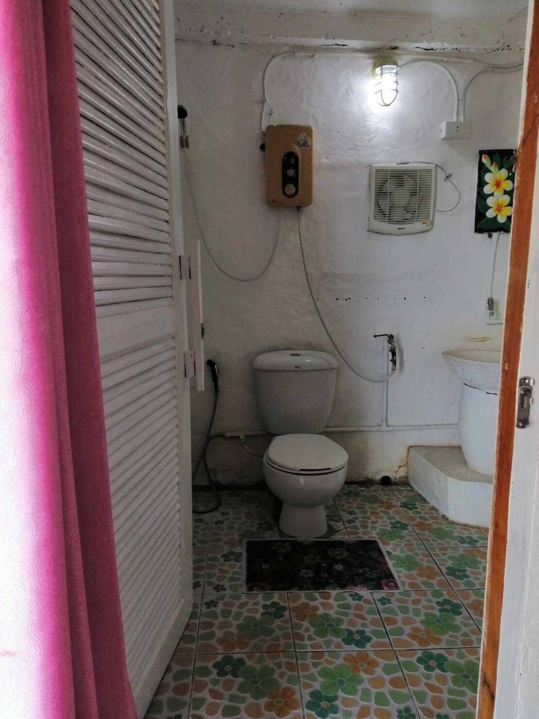 A small bathroom with a toilet, a wall-mounted heater, and a fan.