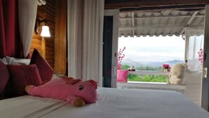 A bed with a pink stuffed toy, white bedding, and a view of greenery and mountains through a balcony. - Ingmhok Country Mountain View Resort (Suan Phueng)