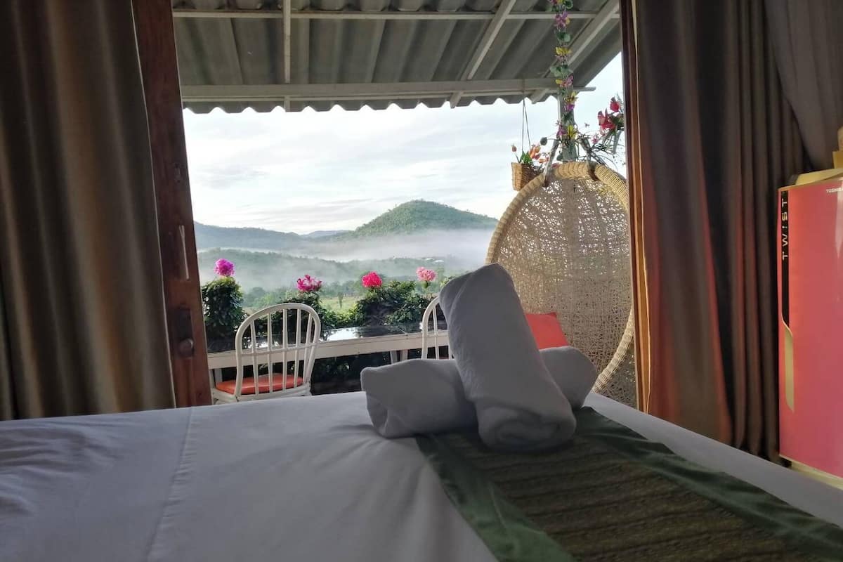 A hotel room with a bed, a small table with chairs, and a view of a mountainous landscape.