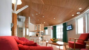 Una sala de estar moderna con un sofá rojo, techo de madera y una cocina al fondo.