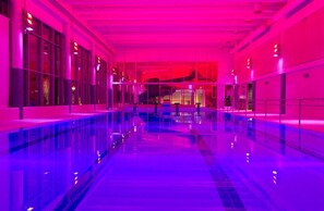A swimming pool with a glass barrier, large windows, and a modern interior design.