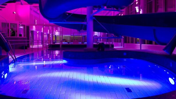 Una piscina interior con un tobogán central, rodeada de un área amplia y techos altos, con arquitectura moderna.