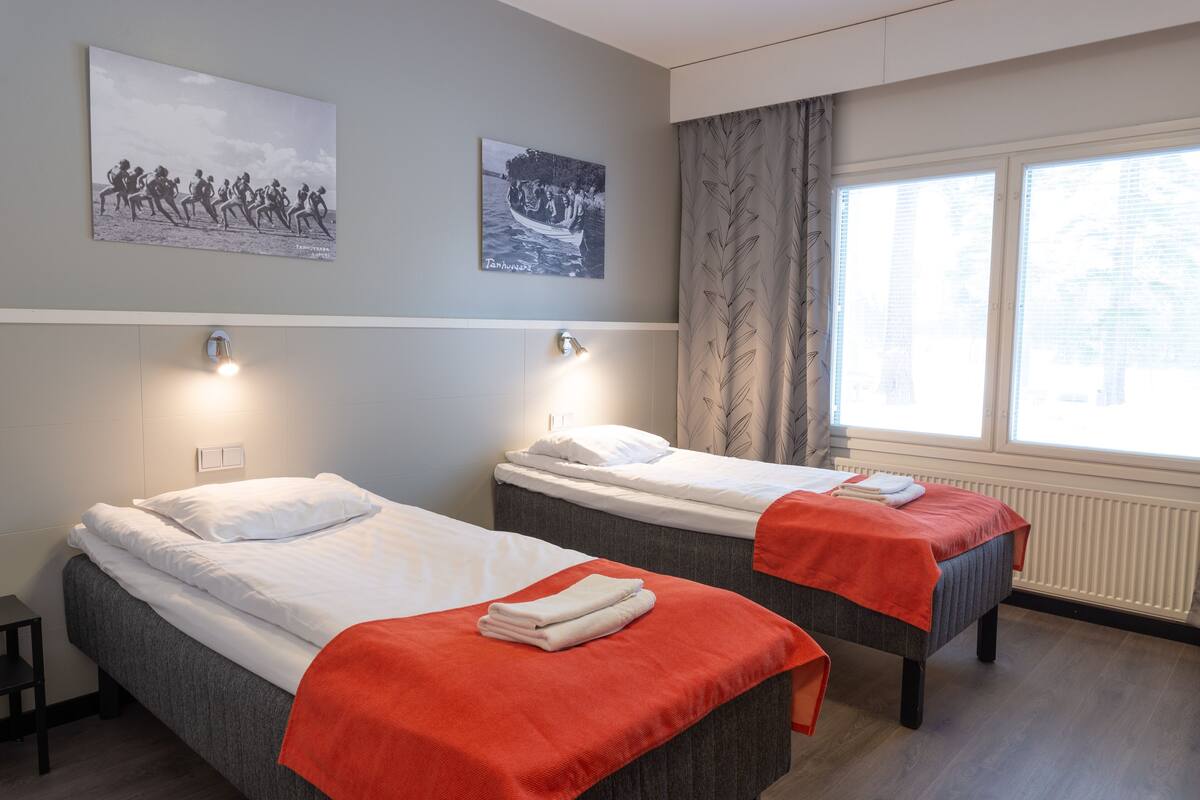 A hotel room with two single beds, a window with curtains, and artwork on the wall.